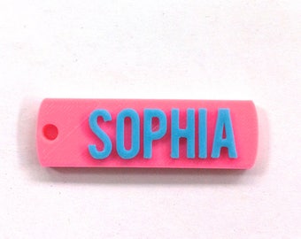 May include: A pink plastic name tag with a blue inscription that reads "SOPHIA".
