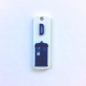 May include: White plastic tag with a blue silhouette of the TARDIS and the letter "D" on it.