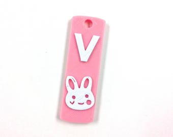 May include: Pink plastic tag with a white letter V and a white bunny face with a smile.