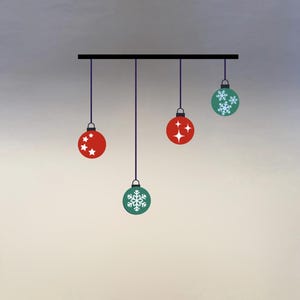 以下が含まれることがあります： 黒い棒から吊り下げられたクリスマスオーナメントのグラフィックイラスト。オーナメントは赤と緑で、星と雪の結晶のデザインが施されています。グラデーションの背景に、紫色の紐で吊り下げられています。