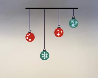 May include: A graphic illustration of Christmas ornaments hanging from a black bar. The ornaments are red and green, with star and snowflake designs. The ornaments are suspended by purple strings against a gradient background.