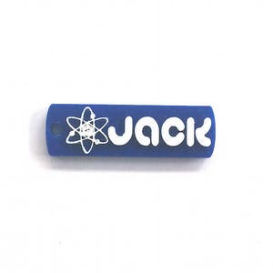 以下が含まれることがあります： 青い長方形のキーホルダー。白いブロック体で「JACK」と書かれています。名前の左側には白い原子記号があります。キーホルダーの端には小さな穴があります。