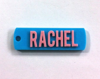 May include: A light blue plastic keychain with a hole for a ring. The name "RACHEL" is printed in pink letters.