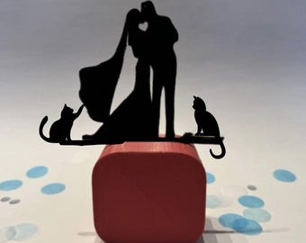 May include: A black silhouette cake topper featuring a kissing couple with a heart-shaped cutout. Two cats are on either side of the couple. The topper sits on a red square base, with blue confetti scattered around.