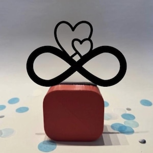May include: A black infinity symbol with two hearts on top, mounted on a red block. The design is set against a white surface with blue confetti, creating a romantic and symbolic aesthetic.