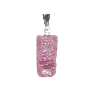 Pode incluir: Um pingente de pedra preciosa rosa bruta de formato retangular, com uma superfície cristalina texturizada e um suporte de metal prateado no topo. A pedra exibe vários tons de rosa profundo e magenta com uma aparência natural.