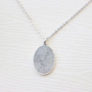 May include: A silver chain necklace with an oval pendant featuring a detailed fingerprint design.