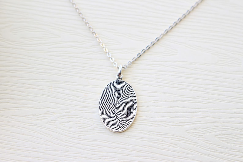 May include: A silver chain necklace with an oval pendant featuring a detailed fingerprint design.
