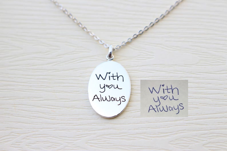 May include: Silver necklace with an oval pendant engraved with the handwritten message "With you Always" and a heart symbol.