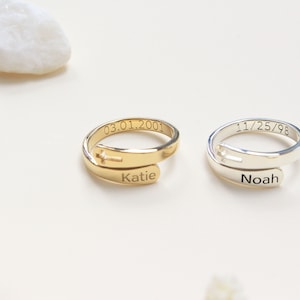 May include: Two personalised rings with a cross design. The gold ring has the name "Katie" and the date "03.01.2001" engraved on it. The silver ring has the name "Noah" and the date "11/25/98" engraved on it.