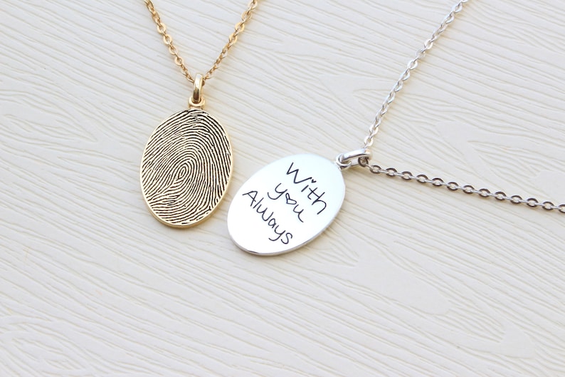 May include: Two silver necklaces with oval pendants. One pendant features a fingerprint design, the other has the inscription "With you Always".