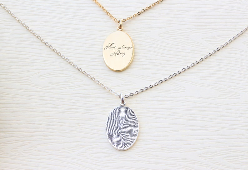 May include: Two silver necklaces with oval pendants. One pendant has a fingerprint design, the other has the handwritten text "Love always, Dadz".