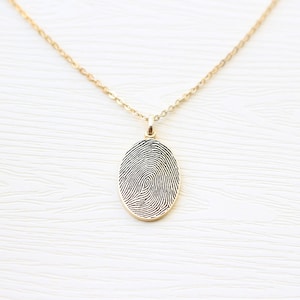 May include: A gold chain necklace with a pendant featuring a detailed fingerprint design.