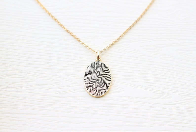 May include: A gold chain necklace with a pendant featuring a detailed fingerprint design.
