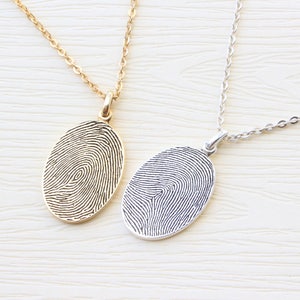 May include: Two silver necklaces with oval pendants featuring a fingerprint design. One necklace has a gold chain and pendant, while the other has a silver chain and pendant.