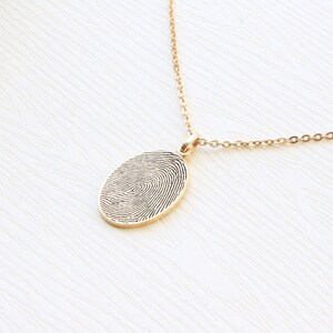 May include: A gold chain necklace with a pendant featuring a detailed fingerprint design.