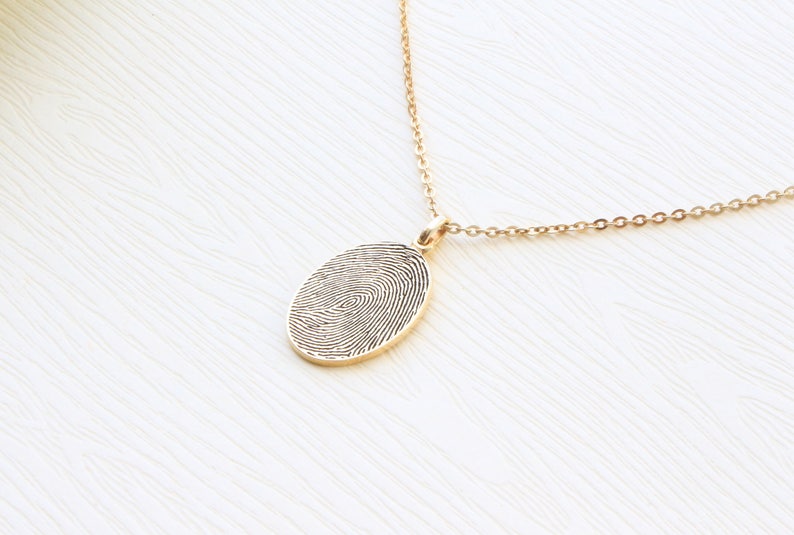 May include: A gold chain necklace with a pendant featuring a detailed fingerprint design.