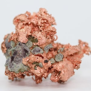 May include: A cluster of copper crystals with a rough, textured surface. The crystals are a reddish-brown color and have a metallic sheen. Some of the crystals are covered in a layer of green and purple mineral deposits.