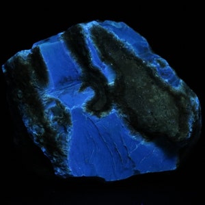 Puede incluir: Una roca grande de forma irregular con una sección gris oscura, casi negra, en un lado. El resto de la roca es de un color azul vibrante, que brilla bajo una luz negra.