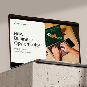 May include: A laptop screen displaying a presentation titled "New Business Opportunity" with a green and orange product launch roadmap chart. The laptop is on a wooden table with a person's hands typing on the keyboard.