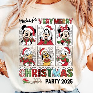 Puede incluir: Camiseta de color marfil con un dise&ntilde;o navide&ntilde;o que presenta a Mickey Mouse, Minnie Mouse, Goofy, Donald Duck y Pluto con gorros y bufandas de Pap&aacute; Noel. El texto dice "Mickey's Very Merry Christmas Party 2025."