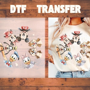 May include: DTF TRANSFER text above a watercolor design featuring Mickey Mouse, Minnie Mouse, Donald Duck, Daisy Duck, Goofy, and Chip and Dale. The design is shown on a clear transfer sheet and a cream-colored t-shirt.