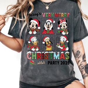Puede incluir: Camiseta gris oscuro con un dise&ntilde;o navide&ntilde;o que presenta a Mickey Mouse, Minnie Mouse, Goofy, Donald Duck y Pluto, todos con gorros y bufandas de Pap&aacute; Noel. La camiseta incluye el texto "Mickey's VERY MERRY CHRISTMAS PARTY 2025".