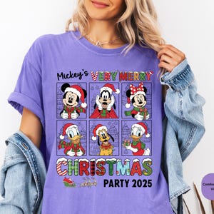 Puede incluir: Camiseta violeta Comfort Colors con un dise&ntilde;o festivo. Presenta a Mickey Mouse, Goofy y Minnie Mouse con gorros de Pap&aacute; Noel. El texto dice "Mickey's Very Merry Christmas Party 2025". El dise&ntilde;o incluye &aacute;rboles de Navidad y cajas de regalo.