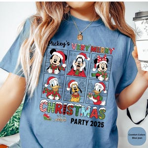 Puede incluir: Camiseta azul vaquero con un dise&ntilde;o de Mickey Mouse, Minnie Mouse, Donald Duck, Goofy y Pluto con ropa navide&ntilde;a. El texto "Mickey's Very Merry Christmas Party 2025" est&aacute; impreso en la camiseta.