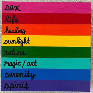 May include: A rainbow-colored wooden sign with the words "sex", "life", "healing", "sunlight", "nature", "magic/art", "serenity", and "spirit" written in black paint.