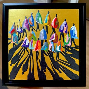May include: A framed painting featuring a group of stylized figures in colorful cloaks walking across a gold background. The figures cast long black shadows. The artwork is framed in a black square frame.