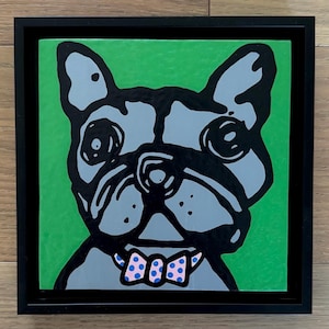 May include: A square framed wall art piece featuring a stylized gray French Bulldog illustration against a vibrant green background. The dog has bold black outlines, large eyes, and wears a light pink bow tie with small blue polka dots.