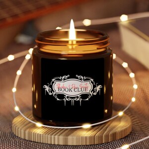 Peut inclure: Une bougie en verre brun avec une étiquette noire qui dit "Readers & Book Scouts Book Club". La bougie est allumée et entourée de lumières féériques blanches.