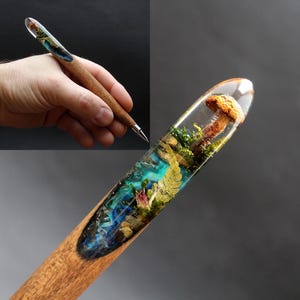 May include: A wooden pen with a clear resin section containing a miniature forest scene with a mushroom, moss, and ferns. The resin is a vibrant blue and green color.