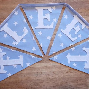 May include: A blue and white star-patterned bunting spelling out "LIFE" in white letters. The bunting consists of triangular flags connected by a white ribbon. The letters are cut out and attached to the flags.