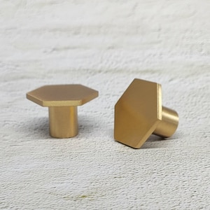 May include: Two gold hexagonal cabinet knobs with a smooth, polished finish.