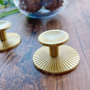 May include: Two gold-toned cabinet knobs with a sunburst design. The knobs are on a wooden surface.