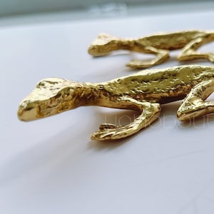 Puede incluir: Dos figuritas de lagarto de color dorado. Los lagartos están detallados con escamas texturizadas y están en posición de carrera.