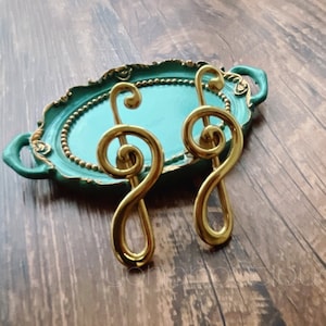 以下が含まれることがあります： ゴールドのトレブルクレフ型の装飾的な引き出しノブが、ゴールドのアクセントが施されたティールグリーンのトレイに乗っています。