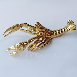 May include: A gold-coloured metal lobster-shaped napkin ring.