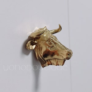 Puede incluir: Una escultura de cabeza de toro de oro con cuernos, una cara detallada y una superficie texturizada.