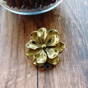 Puede incluir: Una flor de metal de color dorado con cinco pétalos. La flor está sobre una superficie de madera.