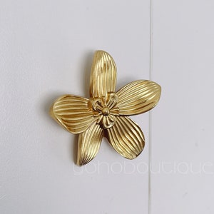 May include: Gold-toned metal flower-shaped cabinet knob with a textured surface.