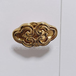 May include: A gold-coloured, cloud-shaped cabinet pull with intricate swirling details. The hardware is mounted on a white surface. The text "yohoboutique" is visible on the lower left.