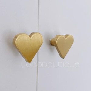 Puede incluir: Dos pomos de armario en forma de corazón de color dorado.