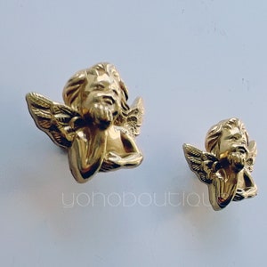 May include: Two gold cherub figurines with wings. The larger cherub is on the left and the smaller cherub is on the right.