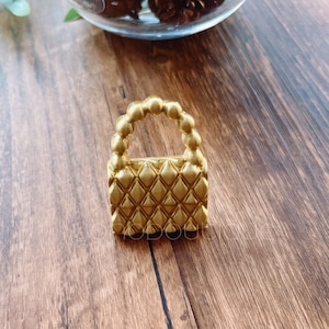 Puede incluir: Un pequeño bolso de mano dorado con un patrón de diamantes y un asa de cuentas.