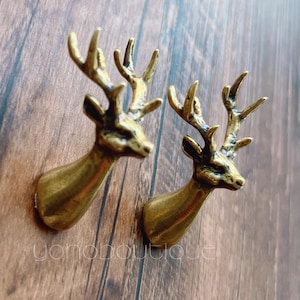 May include: Two bronze-colored deer head wall decor pieces. Each deer head has detailed antlers and a textured surface. The deer heads are mounted on a wooden surface, creating a rustic aesthetic. The overall design is suitable for a cabin or lodge-themed decor.