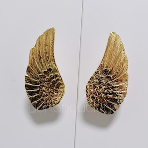 May include: Two gold-colored metal wing-shaped drawer pulls.