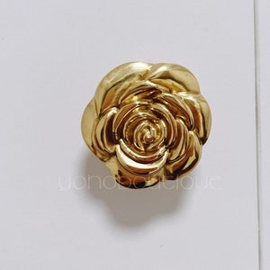 Puede incluir: Un pomo de armario en forma de rosa de color dorado.